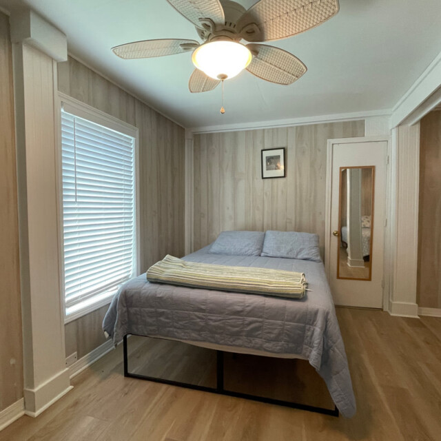 Bedroom with a ceiling fan, bed with blue bedding, a window with blinds, and a mirror on the door.