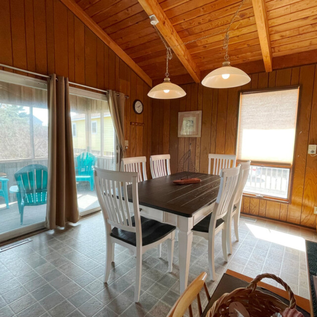 Wood-paneled dining area with a dark table, white chairs, and sliding doors leading to a patio with teal chairs.