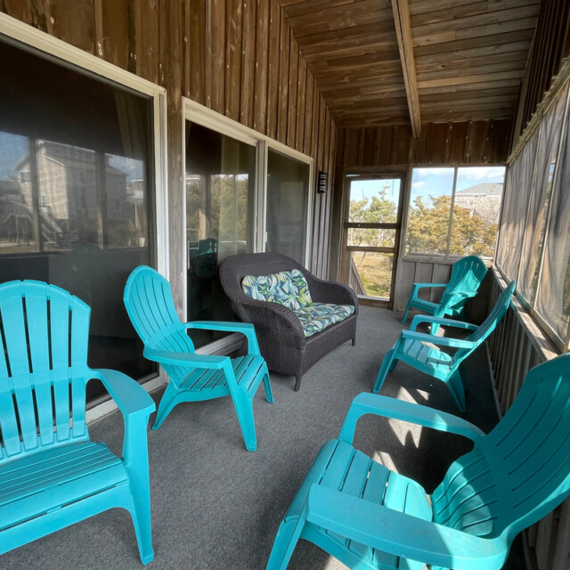 Screened porch with four turquoise chairs, a dark loveseat with cushions, and a small table on a carpeted floor.