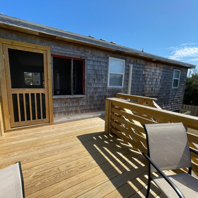 Wooden deck with chairs facing a shingled house, under a clear blue sky.