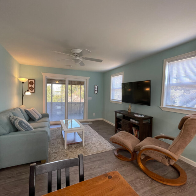 Living room with blue walls, sofa, TV, rocking chair, coffee table, and sliding glass doors leading to a balcony.