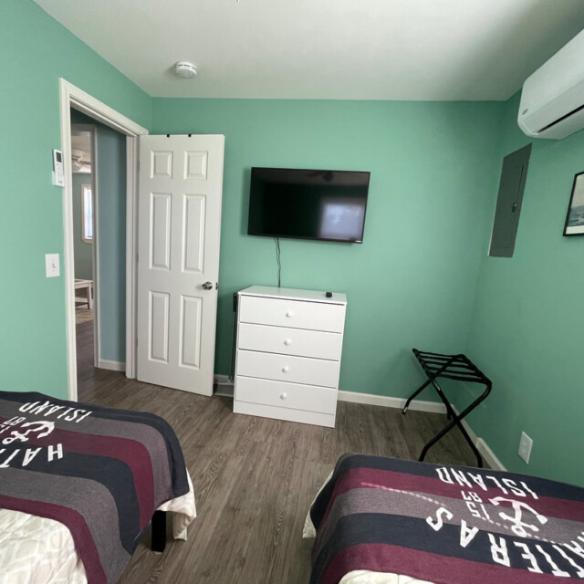 Bedroom with two twin beds, a wall-mounted TV, a white dresser, green walls, and a split air conditioner.