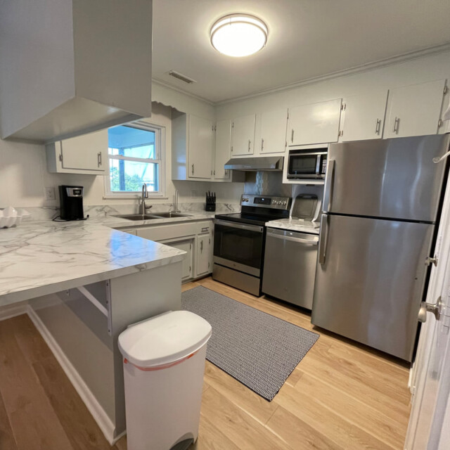 Modern kitchen with stainless steel appliances, marble countertops, white cabinets, and wood flooring.