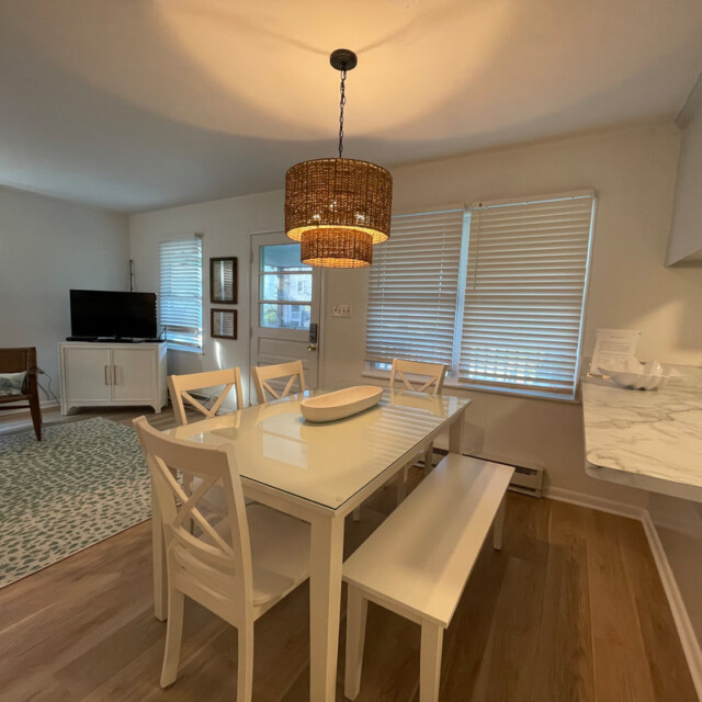 Dining area with white table, chairs, and bench, a woven pendant light, and adjacent living and kitchen spaces.