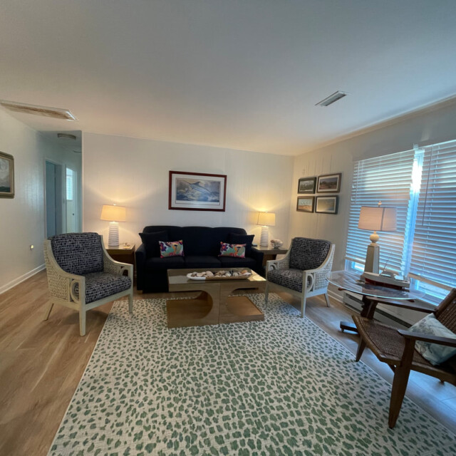 Living room with sofa, two armchairs, coffee table, lamps, wall art, large window with blinds, and a patterned rug.