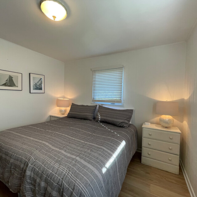 Small bedroom with a double bed, two nightstands with lamps, art on the wall, and a window with blinds.