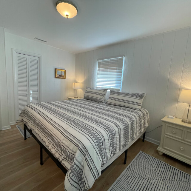 Bedroom with a striped bedspread, two nightstands with lamps, a rug, and a window with closed blinds.
