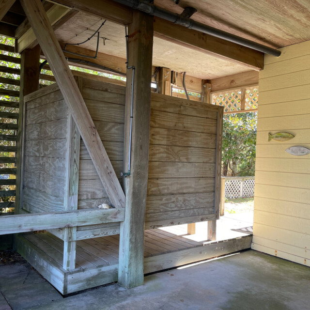 Outdoor wooden shower enclosure beside a yellow building with fish decorations on the wall.