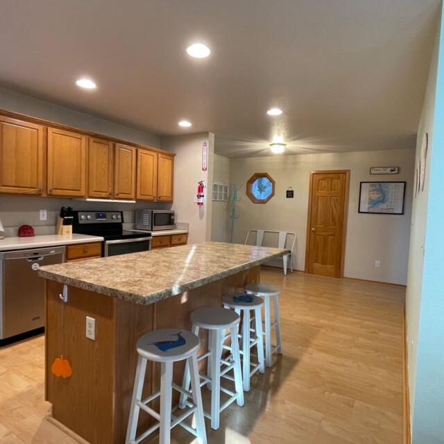 Spacious kitchen with wood cabinets, island with three stools, stainless appliances, and light wood flooring.