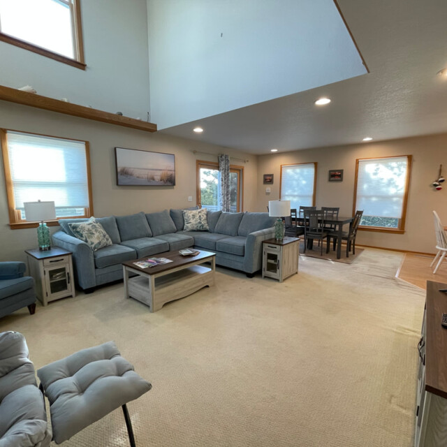 Spacious living room with gray sofas, coffee table, large windows, dining area, and TV in a bright, open-plan home.