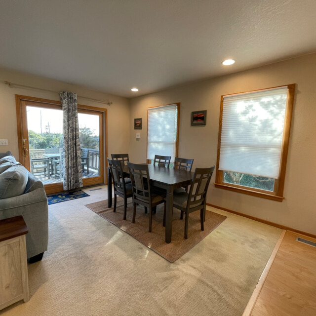 Dining area with a dark wood table and eight chairs, beige walls, large windows, and sliding glass door to outside.