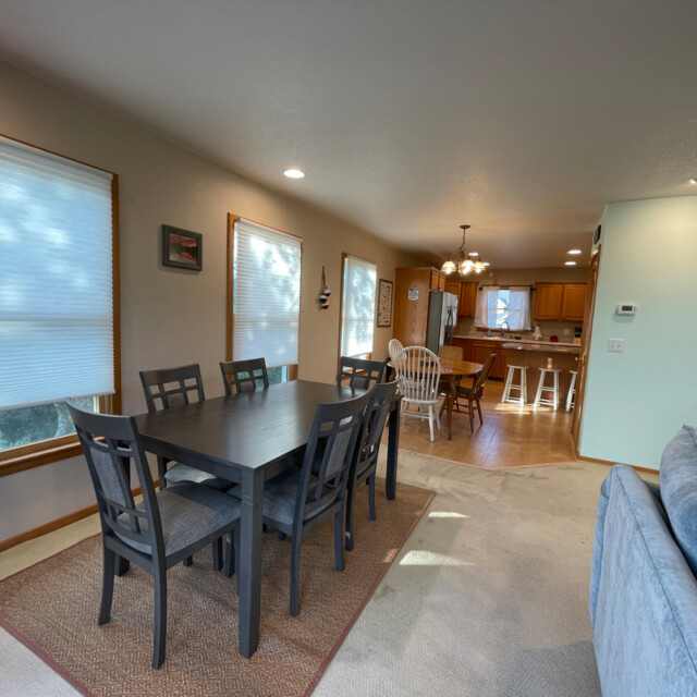 Dining area with a dark wood table and six chairs, adjacent to a kitchen with an island and barstools.