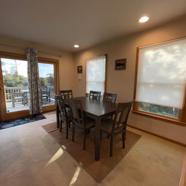 Dining area with six chairs, rectangular table, window blinds, and a view of a deck through glass doors.