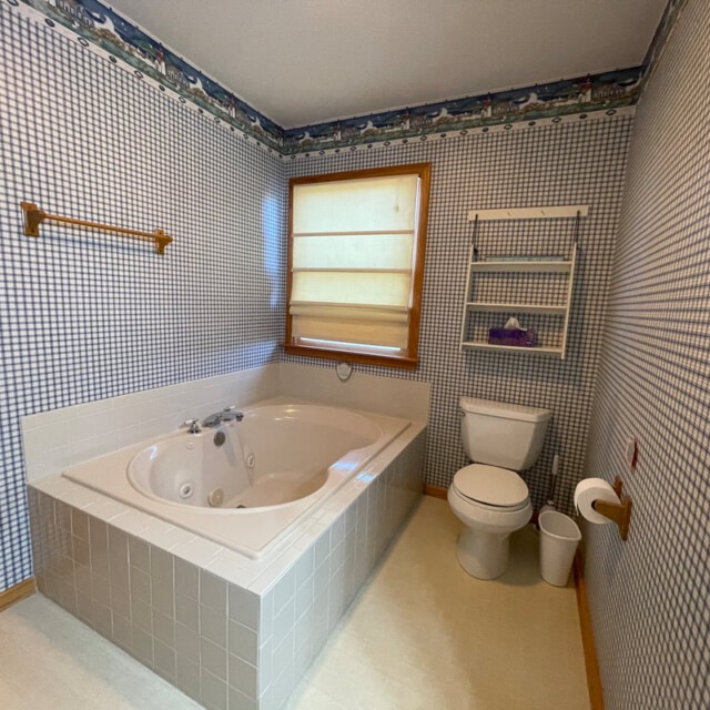 Bathroom with a corner bathtub, toilet, towel rack, and a window with a closed blind.