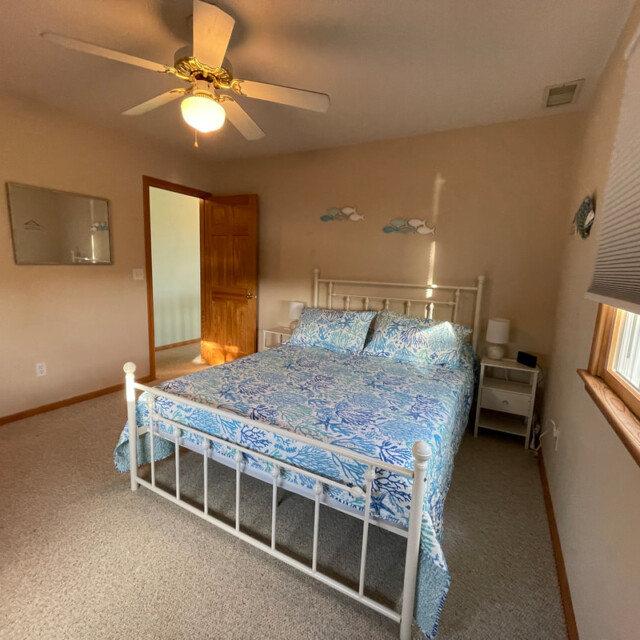 Bedroom with a white metal bed, floral bedding, ceiling fan, nightstands, and window with blinds.