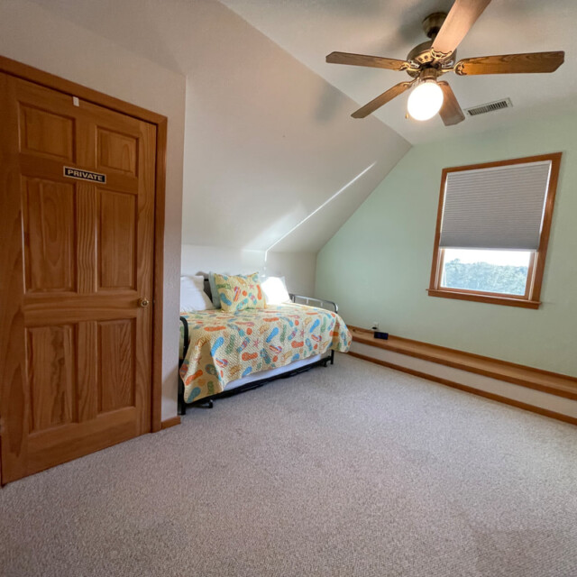 Bedroom with two twin beds, a ceiling fan, carpeted floor, window, and a door labeled “Private.”.