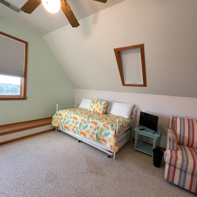 Bedroom with a daybed, colorful bedding, a striped chair, small TV on a nightstand, and two windows.