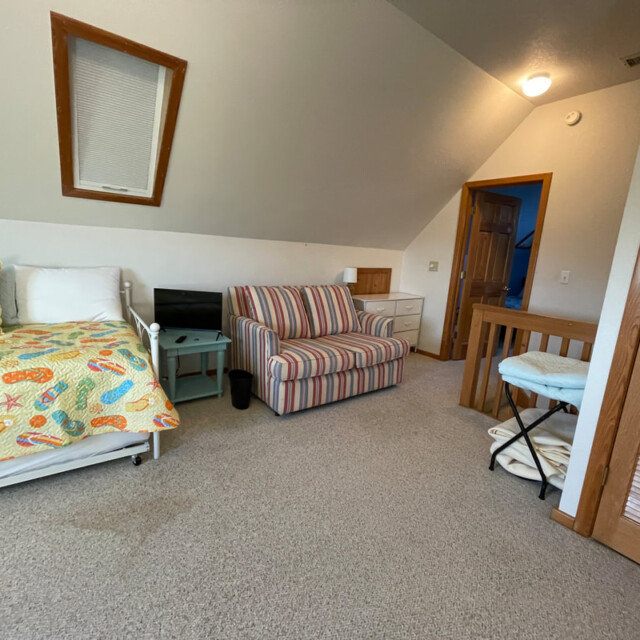 Bedroom with a single bed, striped armchair, small TV, desk, and open closet under a sloped ceiling.