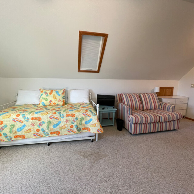 Room with a daybed with a colorful quilt, a striped armchair, side table, and slanted ceiling with a skylight.