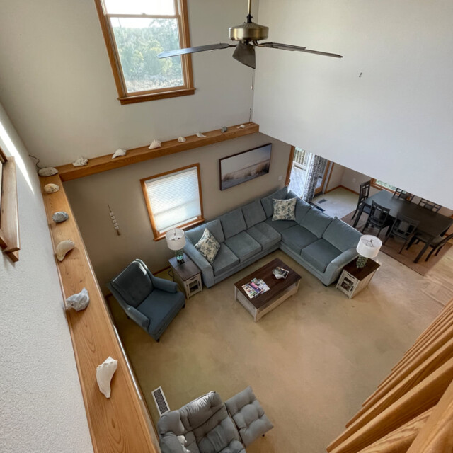 View of a living room with a sectional sofa, coffee table, armchairs, and dining area, seen from an upper floor.