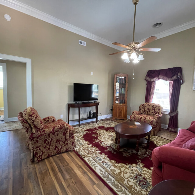 Living room with red furniture, patterned rug, TV, glass cabinet, ceiling fan, and view into a bathroom.
