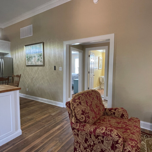 Red patterned armchair in a living area with view of kitchen, hallway, and a partially visible bathroom.