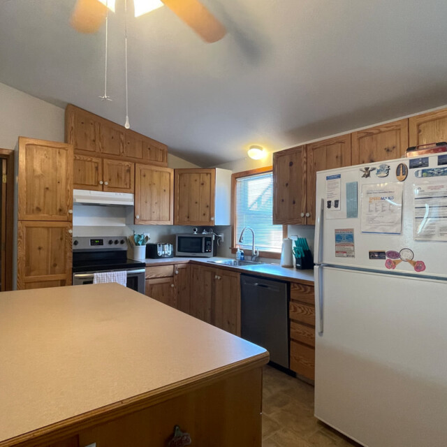 Kitchen with wooden cabinets, white appliances, an island countertop, and a window letting in natural light.