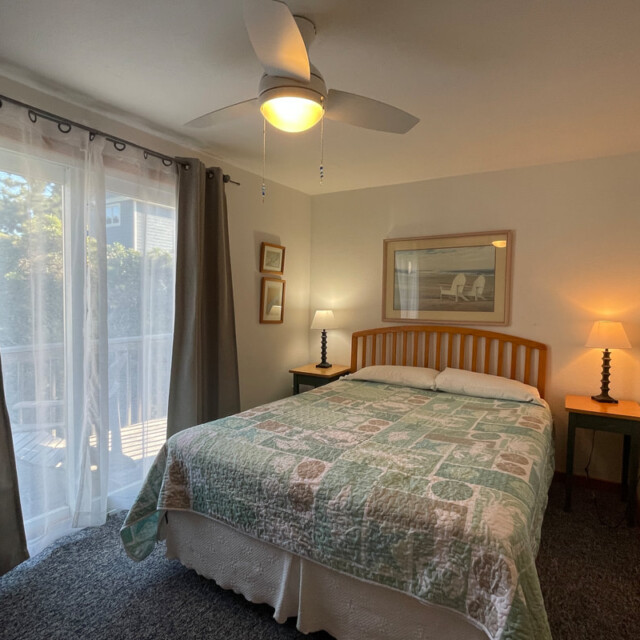 Bedroom with double bed, two bedside tables with lamps, framed art, and sliding doors with sheer curtains.