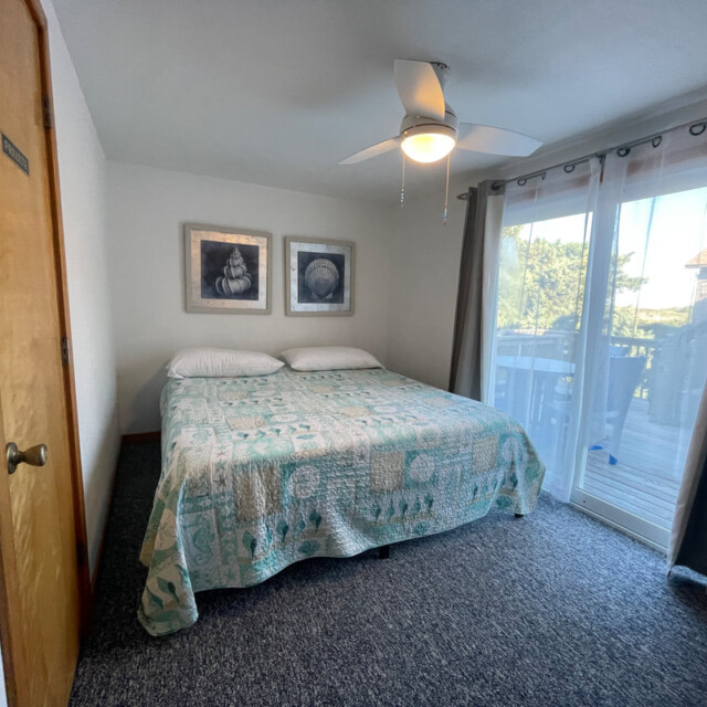 Bedroom with a double bed, ceiling fan, wall art, and sliding glass doors leading to a balcony with outdoor view.