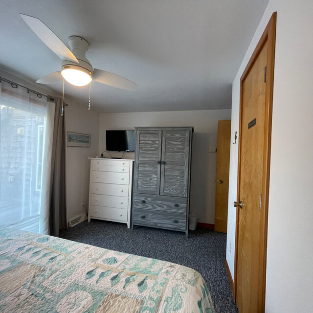 Bedroom with a ceiling fan, bed, dresser, armoire, TV, window with curtains, and a wooden door.