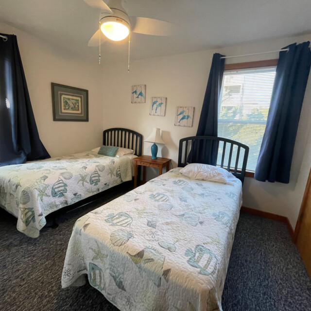 Bedroom with two twin beds, blue and white decor, a small nightstand, and windows with blue curtains.