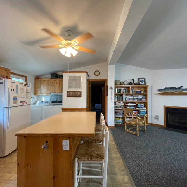 Kitchen with island and stools, adjoining laundry area, living space with fireplace, shelves, and mounted fish decor.