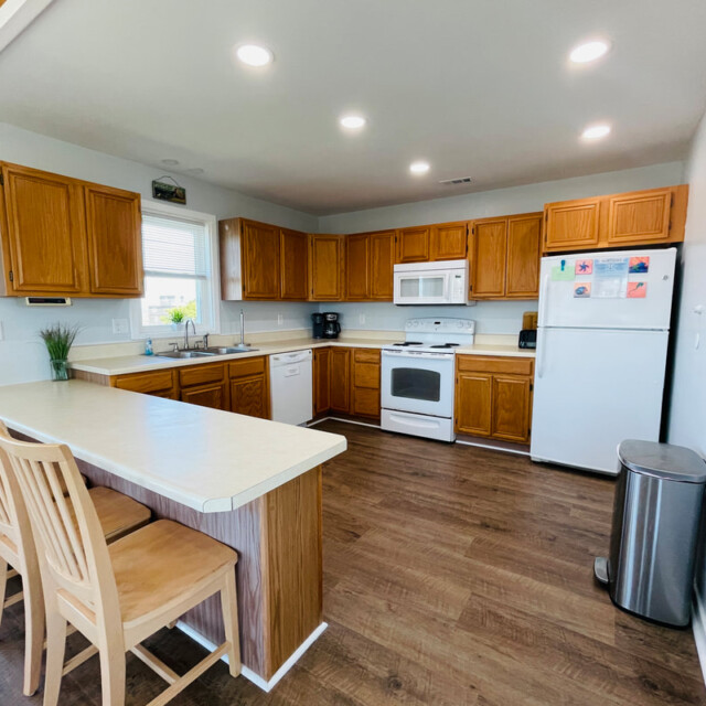 Spacious kitchen with wood cabinets, white appliances, a large counter with three chairs, and hardwood floors.