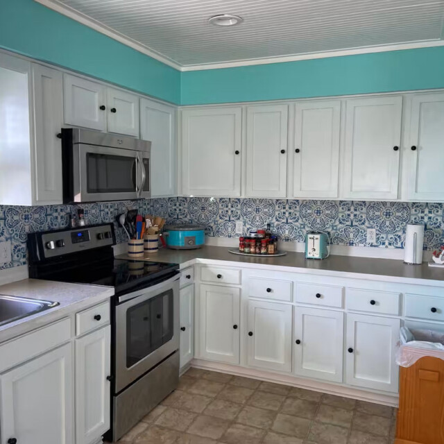 Kitchen with white cabinets, blue walls, patterned backsplash, stainless appliances, and various countertop items.