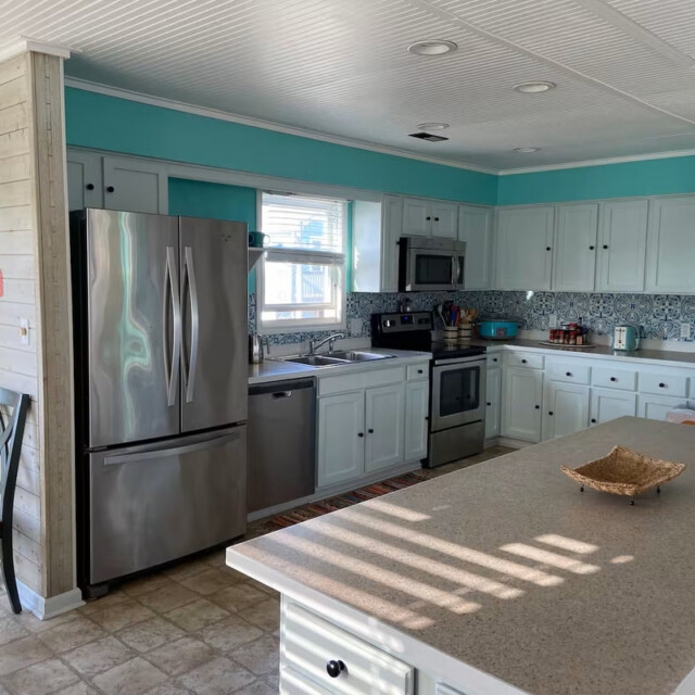 Modern kitchen with white cabinets, stainless steel appliances, and turquoise walls, lit by natural sunlight.