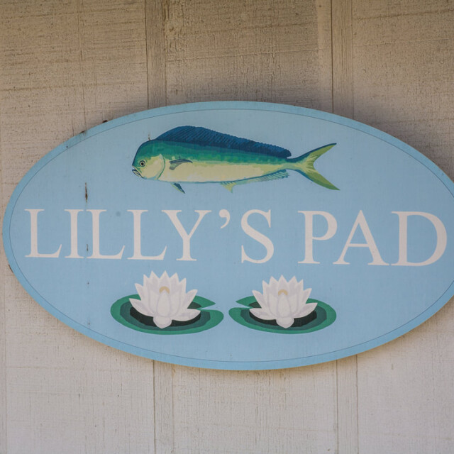 Oval sign reading “LILLY’S PAD” with a fish and two water lilies on a light blue background, mounted on a wall.