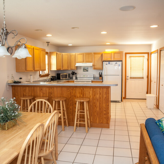 Kitchen and dining area with wood cabinets, a counter with stools, dining table, white appliances, and tiled floor.