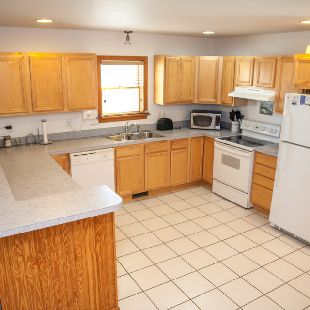 Bright kitchen with light wood cabinets, white appliances, tiled floor, and a U-shaped counter with stools.