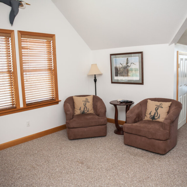 Two brown armchairs with anchor pillows sit by a window in a carpeted room with nautical decor.