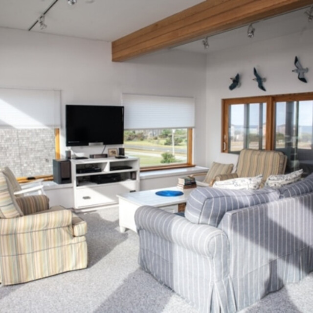 Bright living room with striped sofas, TV, coffee table, wall art, and large windows showing an outdoor view.