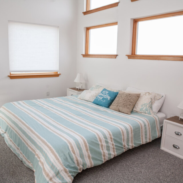 Bedroom with a striped bedspread, two nightstands, three high windows, and a small desk with a chair in the corner.