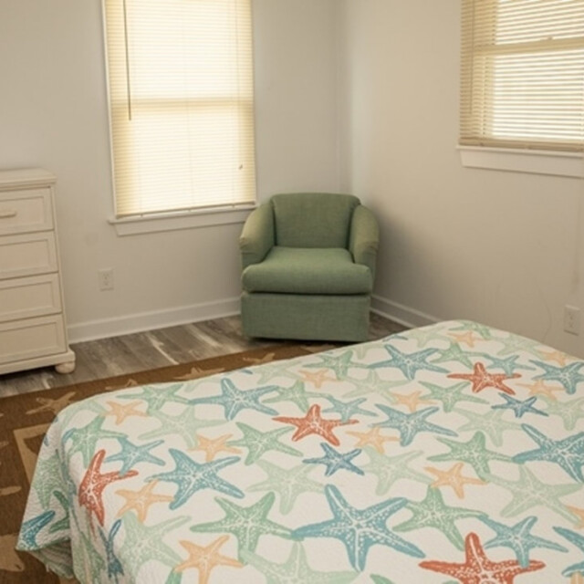 Bedroom with a starfish-patterned bedspread, green chair, white dresser, and windows with blinds.