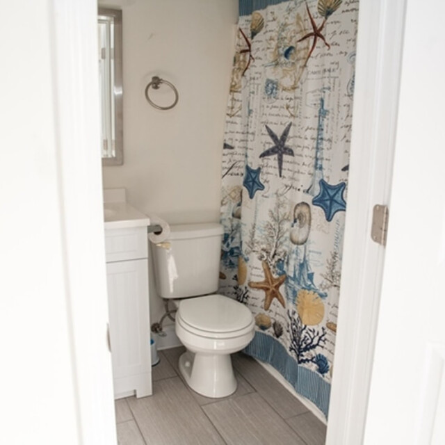 Small bathroom with white toilet, sink, and a shower curtain featuring a nautical and sea life pattern.