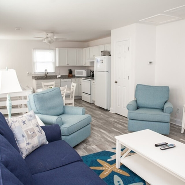 Bright living room with blue furniture, white kitchen, dining table, and two lamps on side tables.